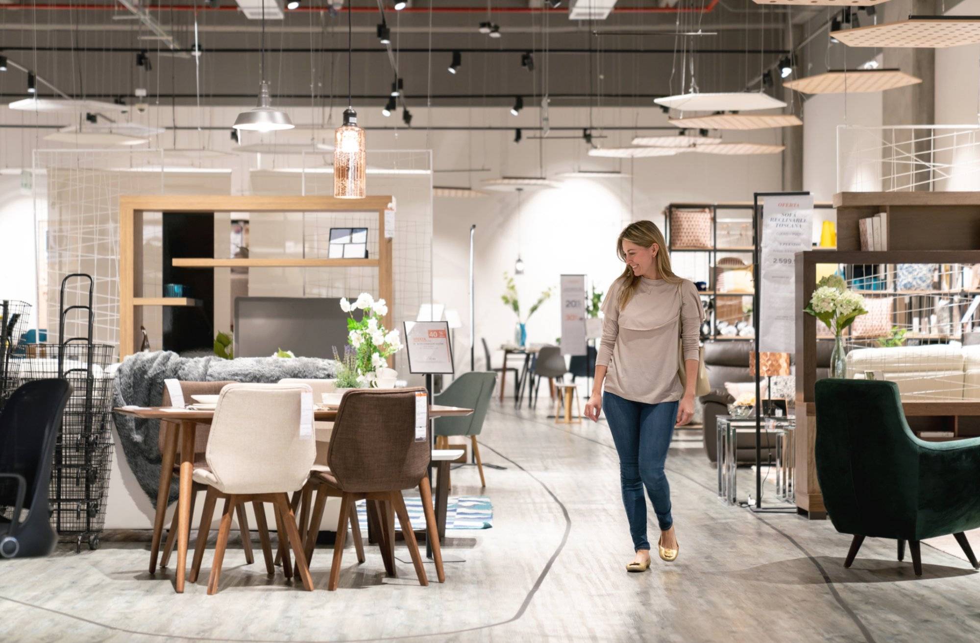 Happy woman shopping at a furniture store and looking at a dining room while smiling - lifestyle concepts